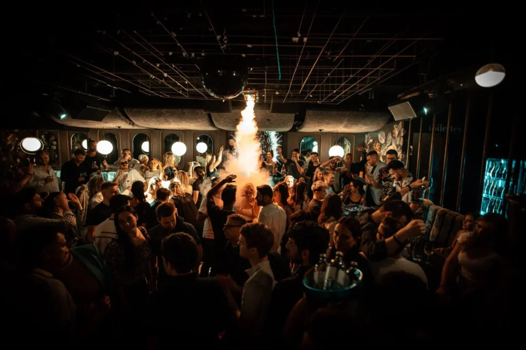 Volle Tanzfläche mit Feuerfontäne bei einer Clubnacht im Le Jardin Linz, umgeben von Gästen, Musik und Flaschenservice.